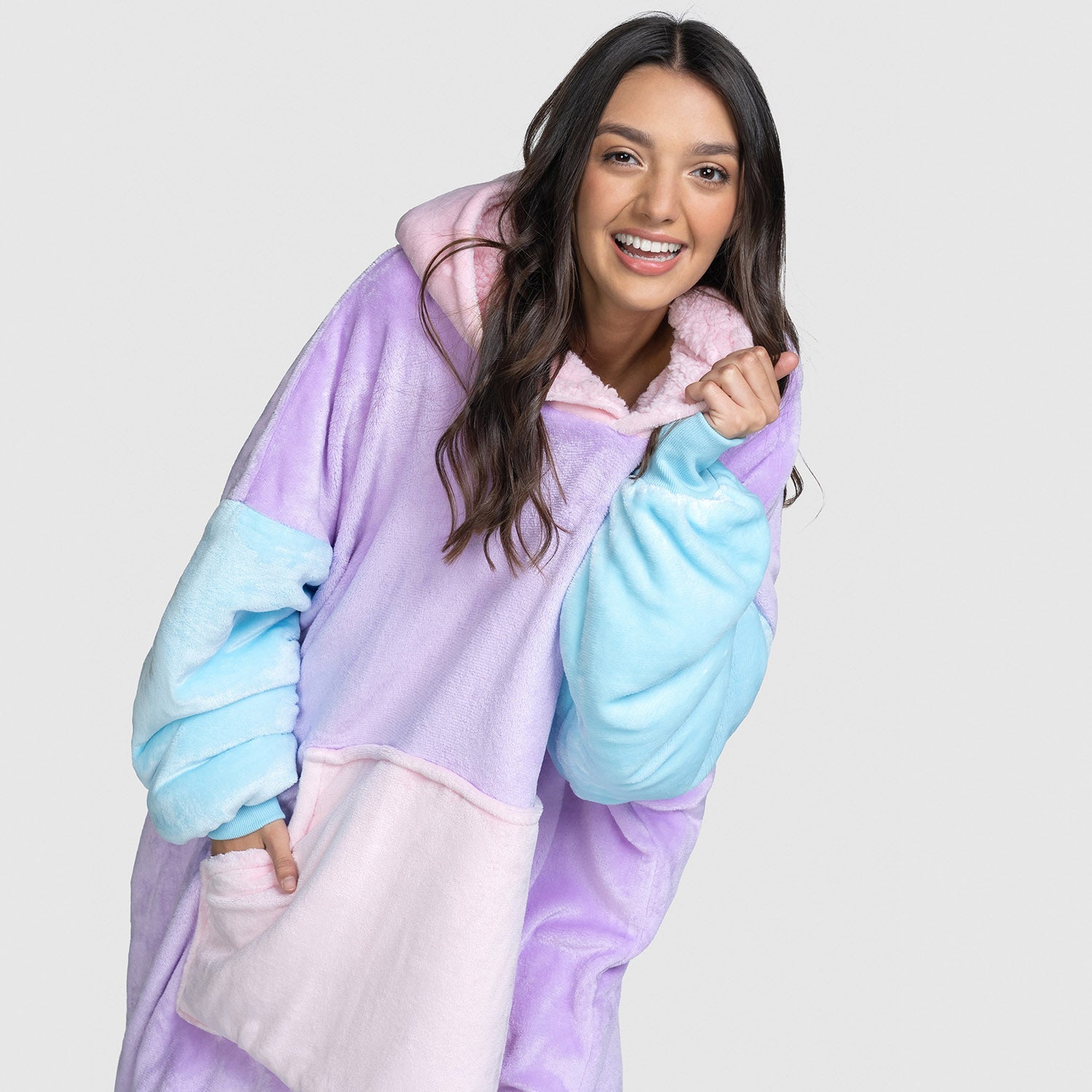 Woman with long dark hair smiling, wearing a pastel color-blocked oversized hoodie with purple, blue, and pink sections, hands in pockets. size: Gracie is 5' 9" wearing a size S/M