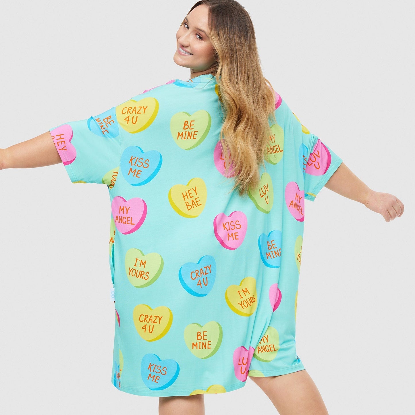 Woman wearing a light blue dress with colorful love heart candy prints including phrases: CRAZY 4 U, BE MINE, KISS ME, HEY BAE, MY ANGEL, I'M YOURS, LUV U