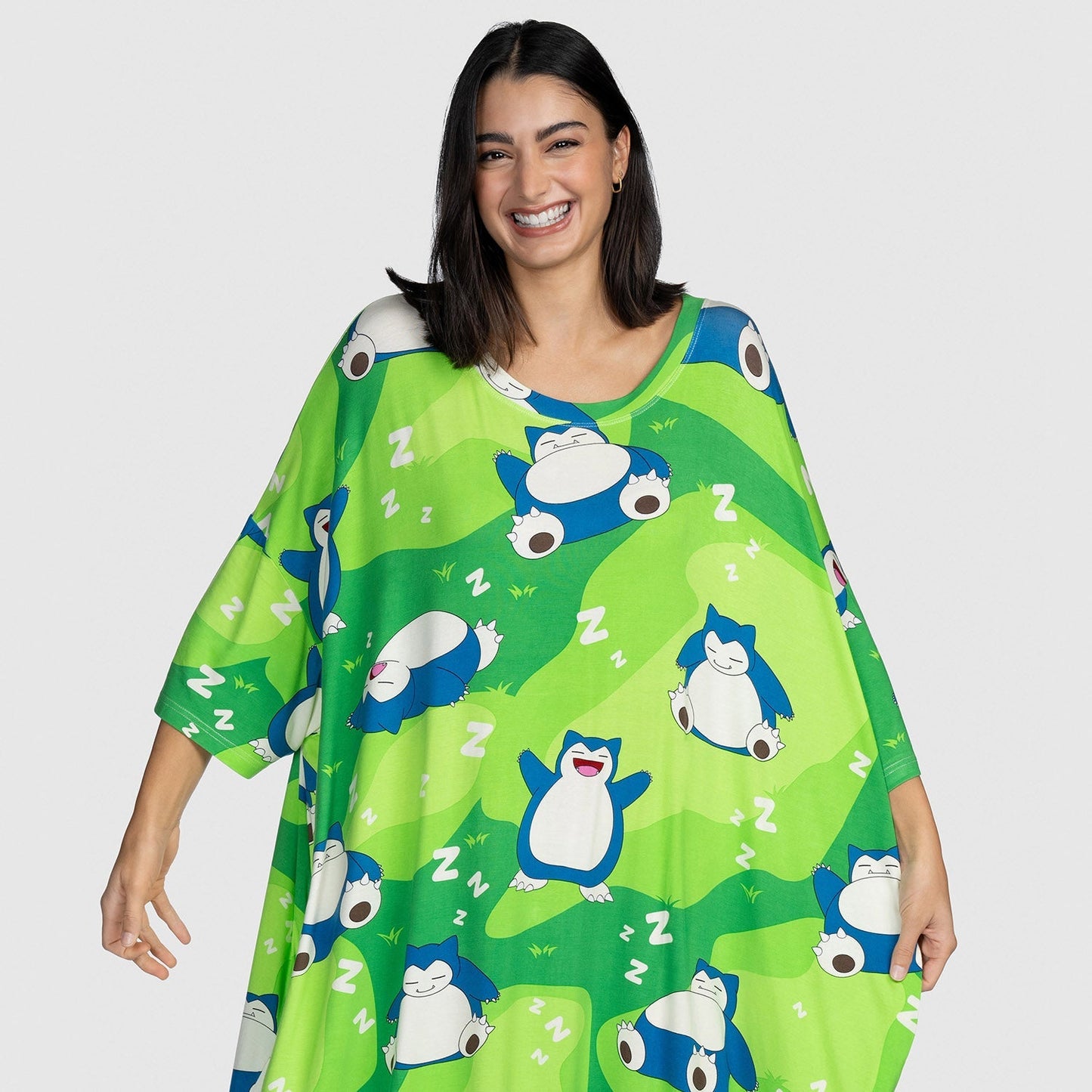 Woman smiling and wearing a green garment patterned with sleeping Pokémon Snorlax characters and white 'Z' symbols.