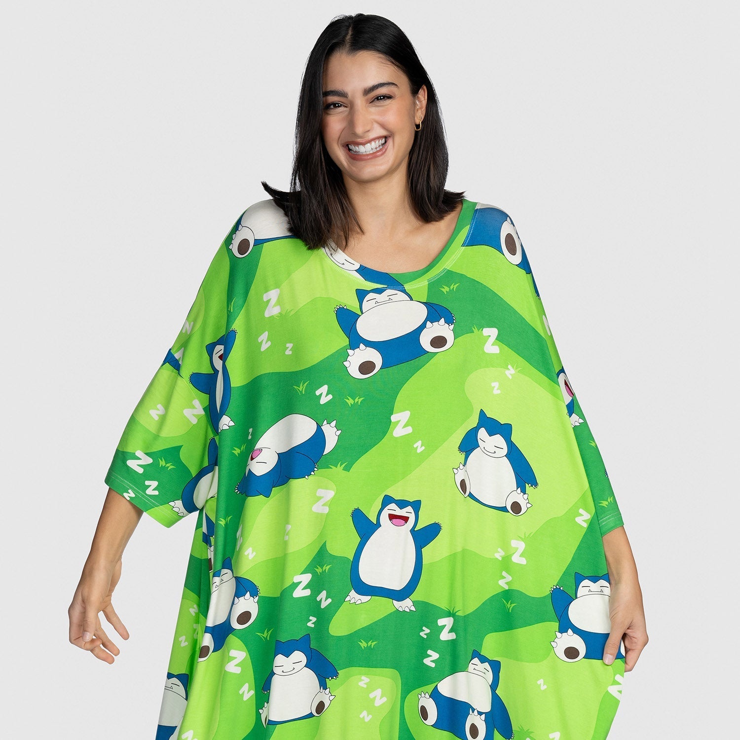 Woman smiling and wearing a green garment patterned with sleeping Pokémon Snorlax characters and white 'Z' symbols.