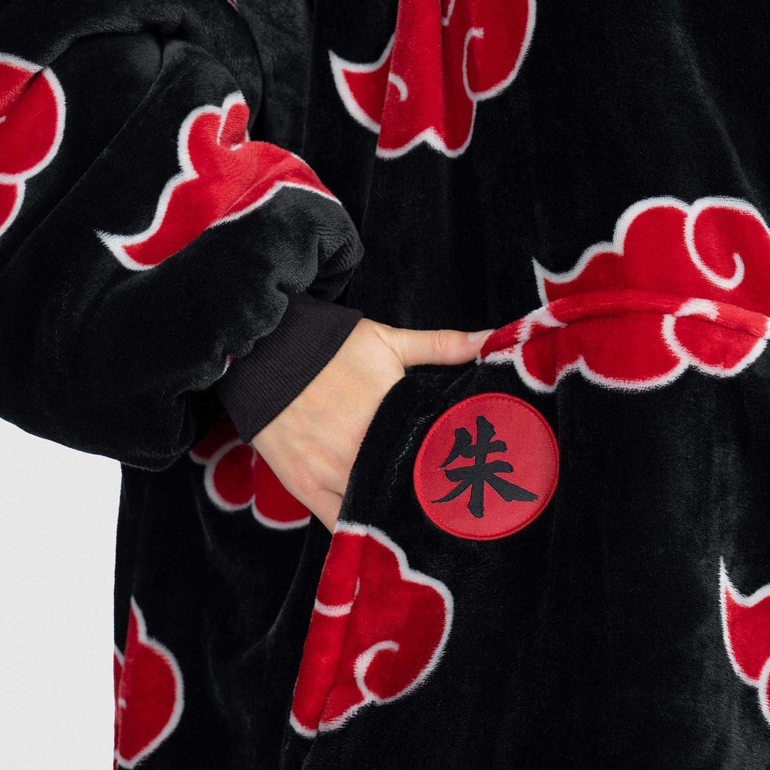 Hand in pocket of black garment with red Akatsuki cloud patterns and a red circular patch with Japanese character 朱