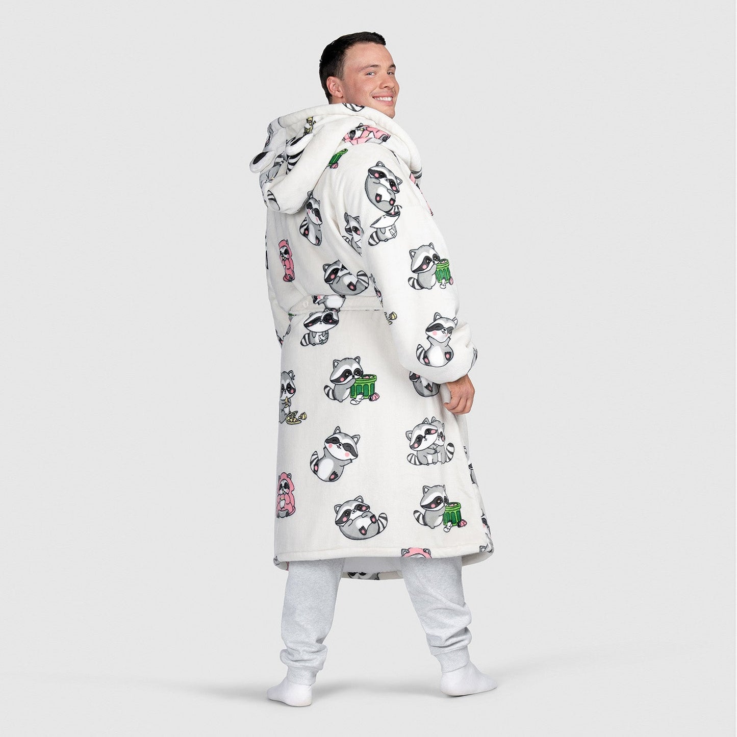 Man wearing a white hooded robe with cartoon raccoon illustrations all over it, smiling and looking over his shoulder.