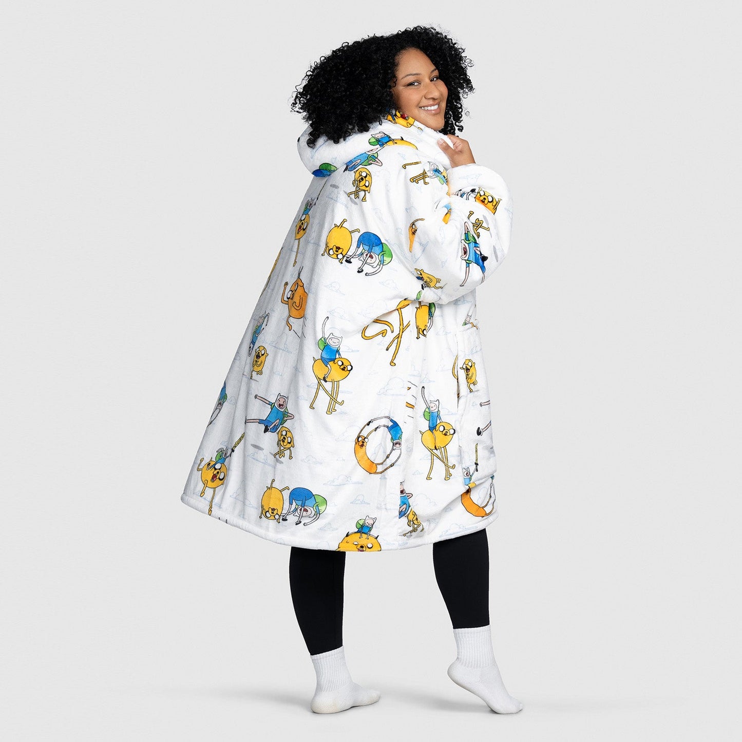 Woman with curly hair wearing a white hooded coat with colorful cartoon character prints, smiling and looking over her shoulder. size: Aisha is 5'3