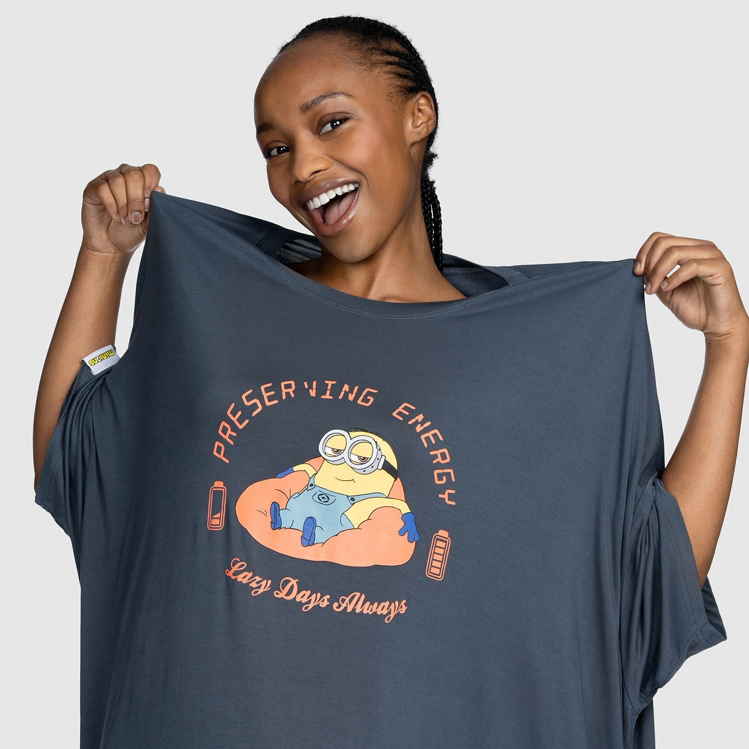 Woman holding a dark shirt with a Minion character and the text 'PRESERVING ENERGY Lazy Days Always' printed on it.