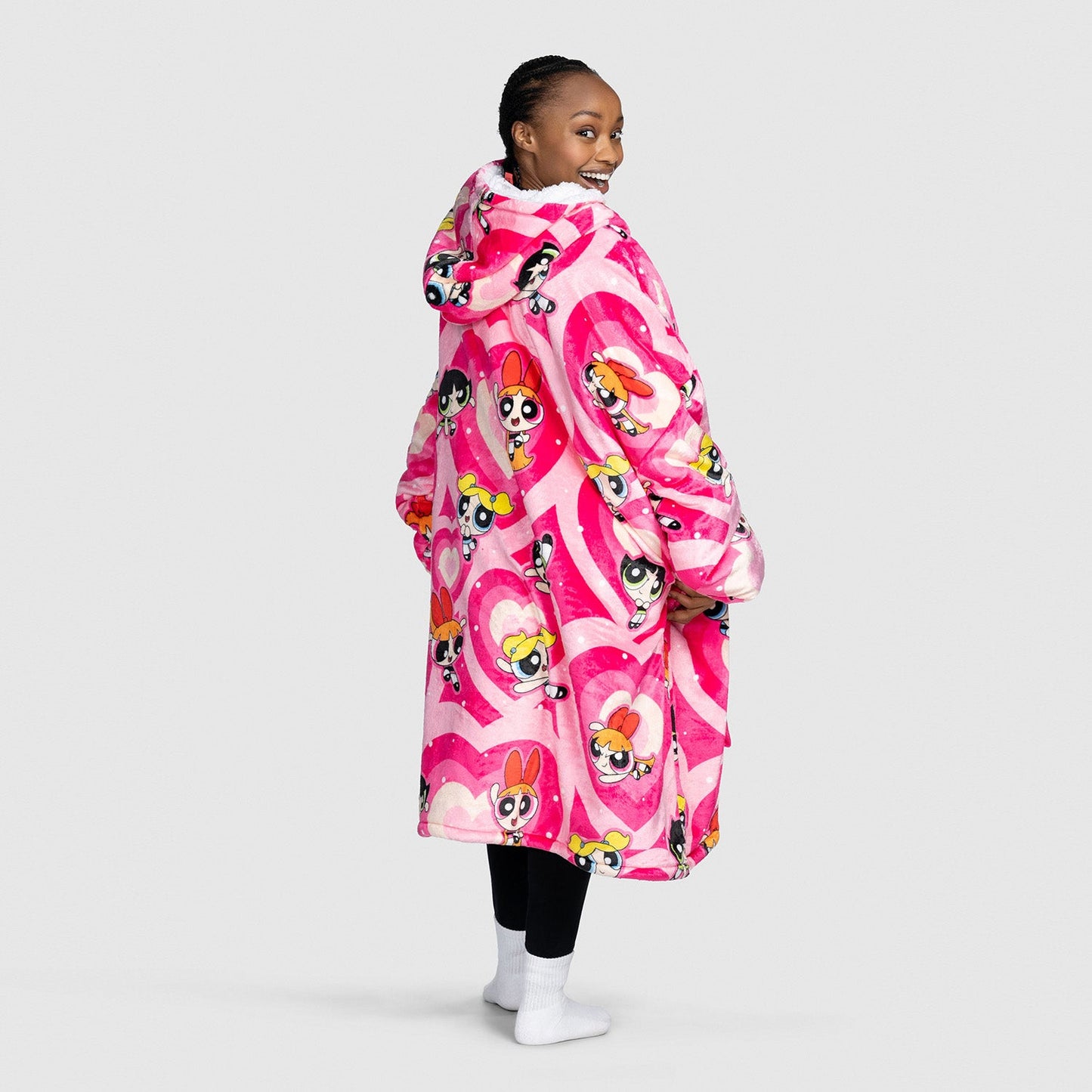 Woman wearing a pink oversized hoodie blanket featuring Powerpuff Girls characters in heart shapes