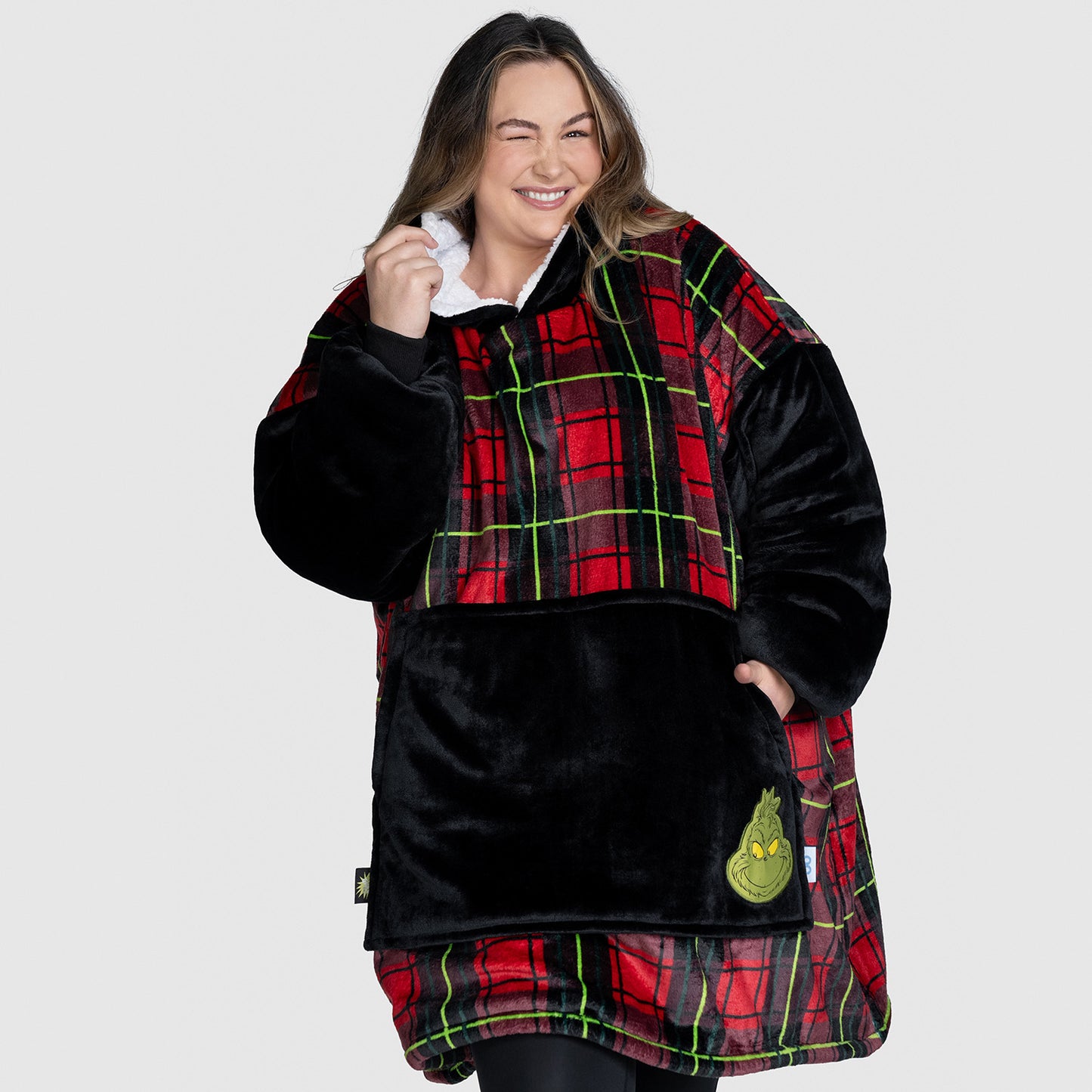 Woman wearing an oversized red and black plaid fleece with black sleeves and a Grinch face patch on the front pocket