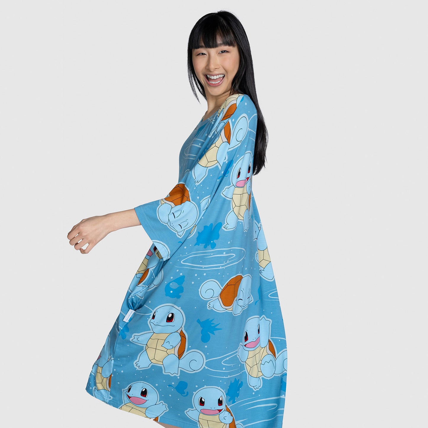 Woman smiling and posing wearing a blue dress patterned with multiple Squirtle Pokémon characters from Pokémon.