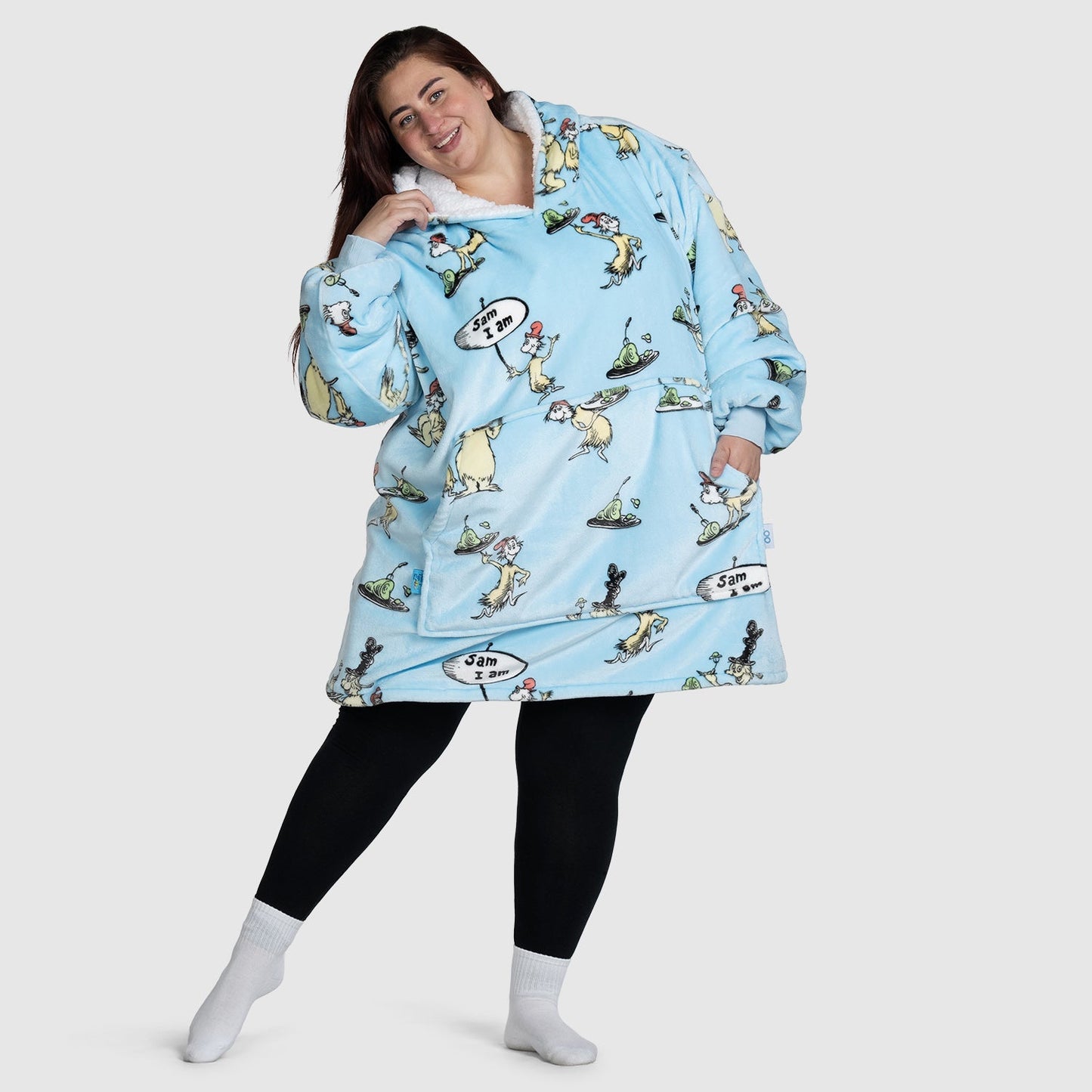 Woman standing wearing an oversized light blue hoodie with cartoon characters and speech bubbles, black leggings, and white socks. Text on image: