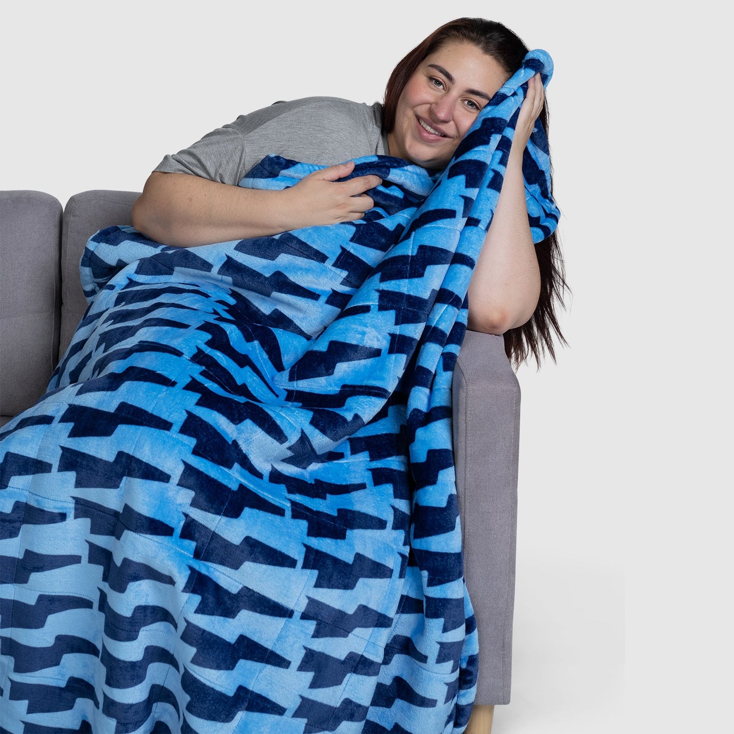 Woman sitting on a couch wrapped in a blue blanket with a geometric pattern