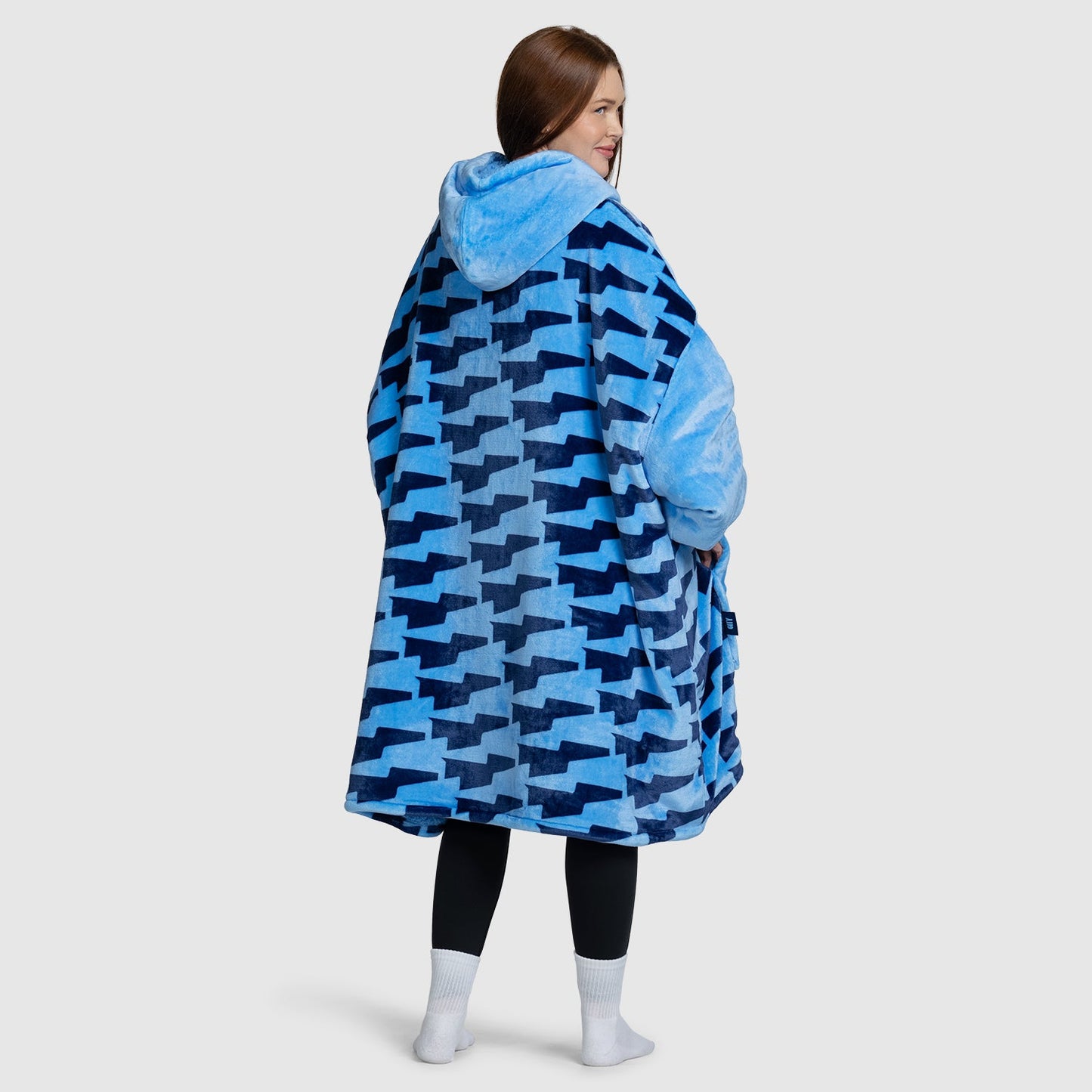 Model wearing a blue patterned oversized hoodie blanket, viewed from the back. Model is 5 feet 7 inches tall and wears size OOD. size: Kat is 5'7