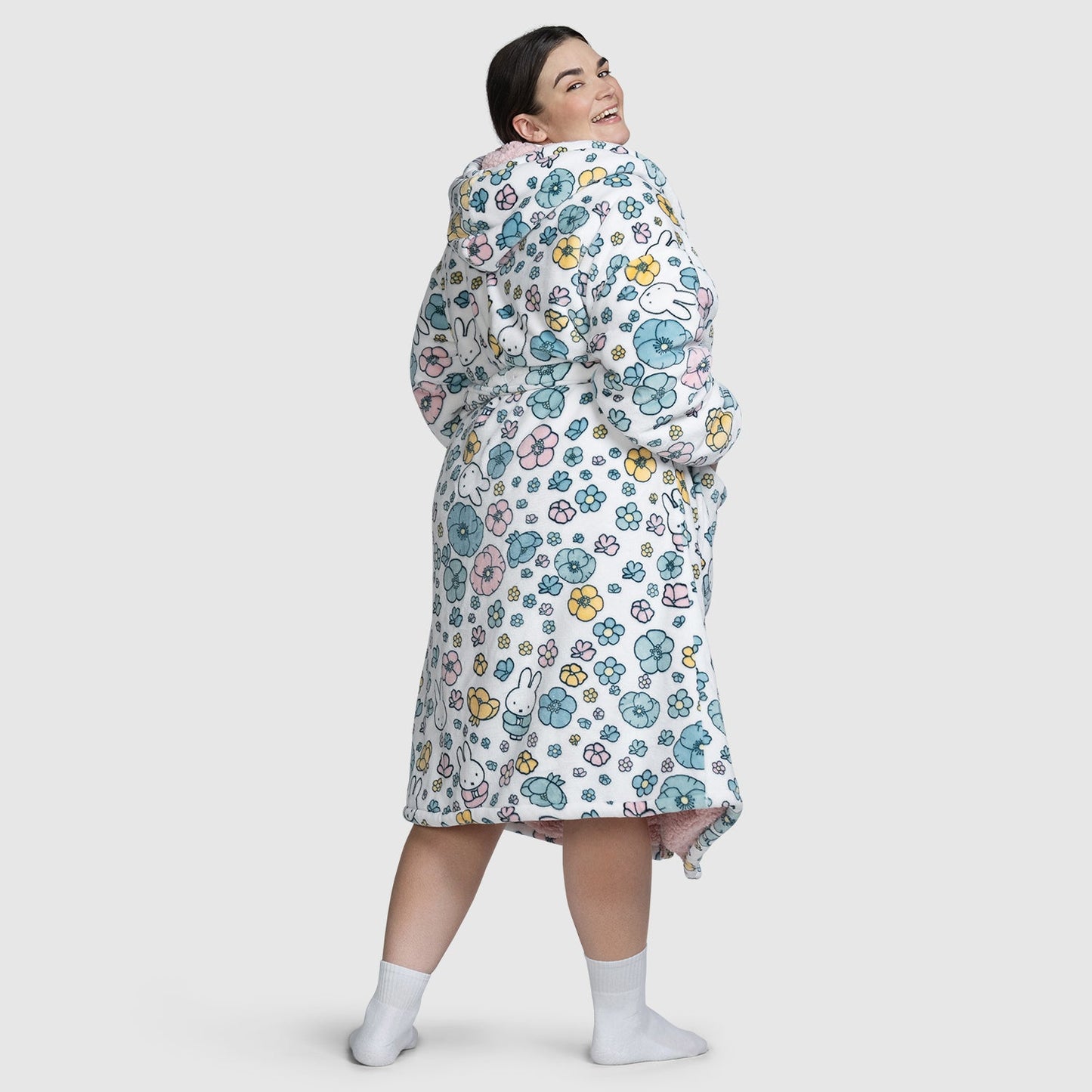 Woman wearing a white robe with colorful floral and character patterns, viewed from the back, smiling over her shoulder.