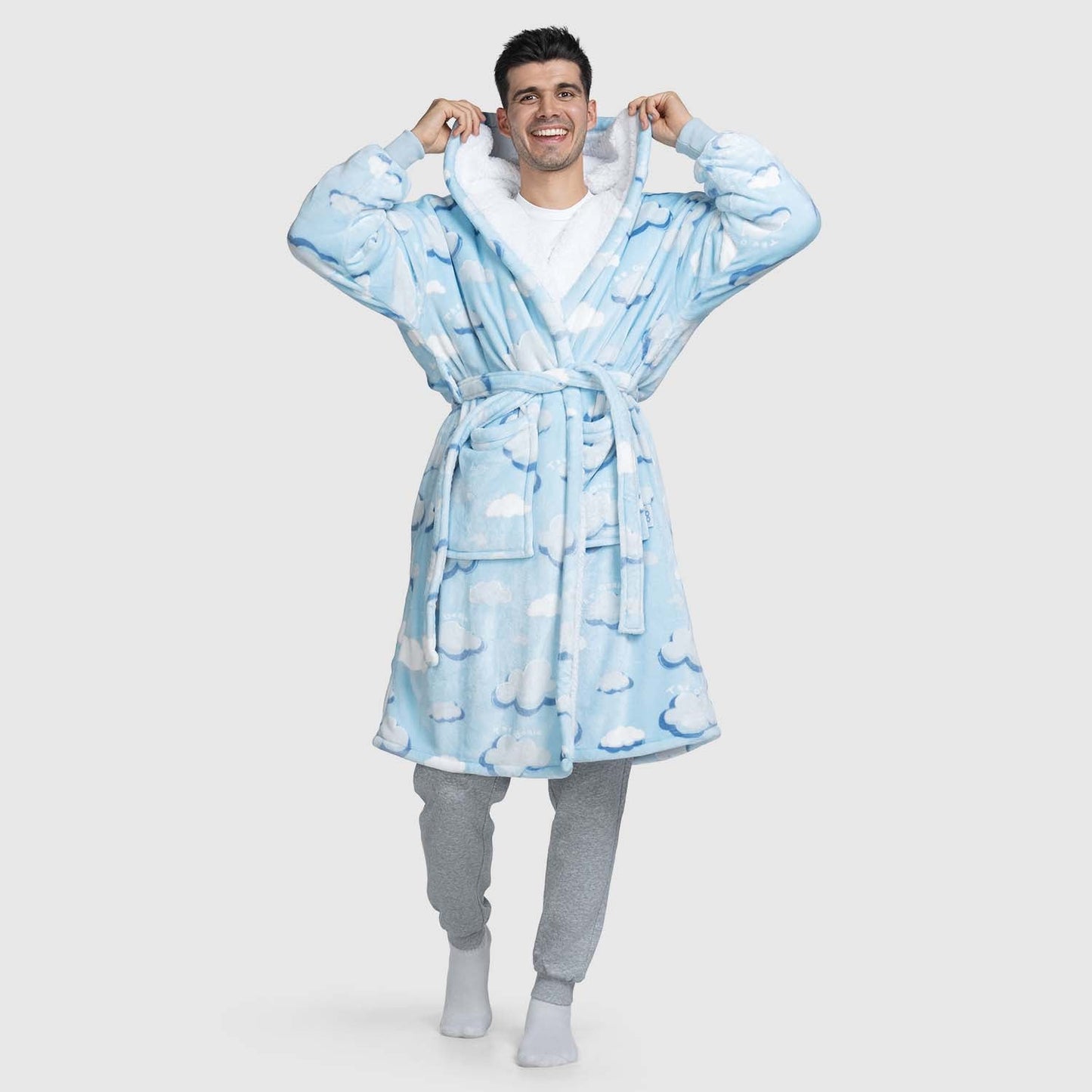 Smiling man wearing a blue robe with white cloud patterns, holding the hood near his face.