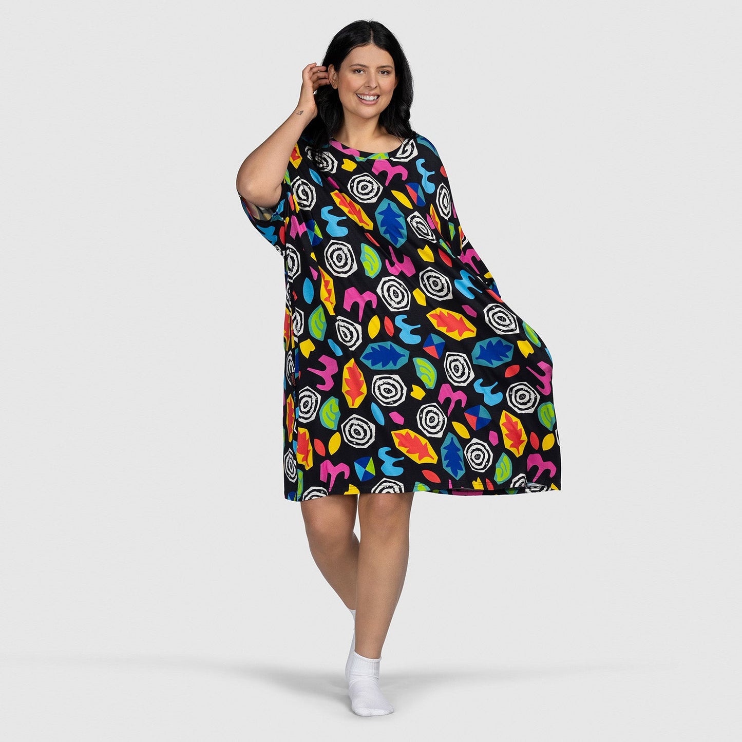 Woman smiling and posing in a colorful patterned dress with abstract shapes on a light gray background