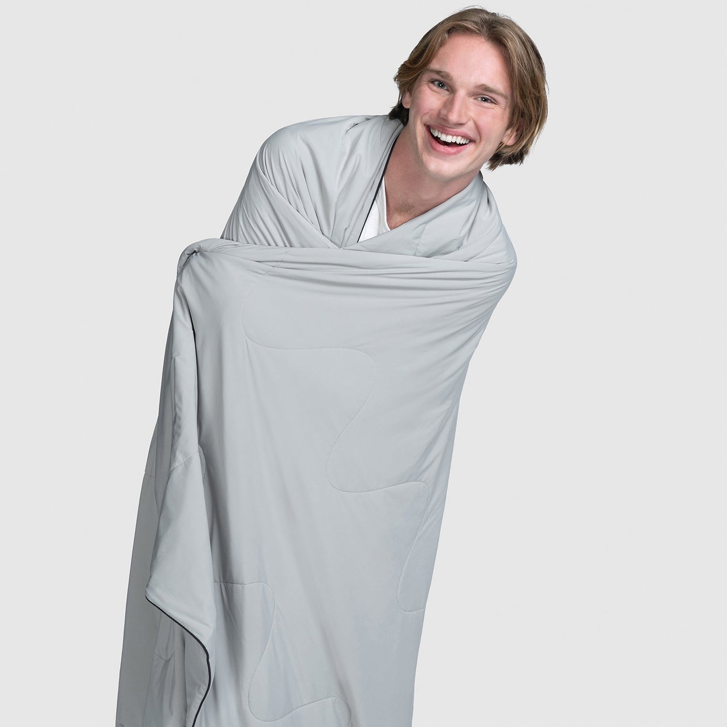 Smiling young man wrapped in a grey blanket against a plain background
