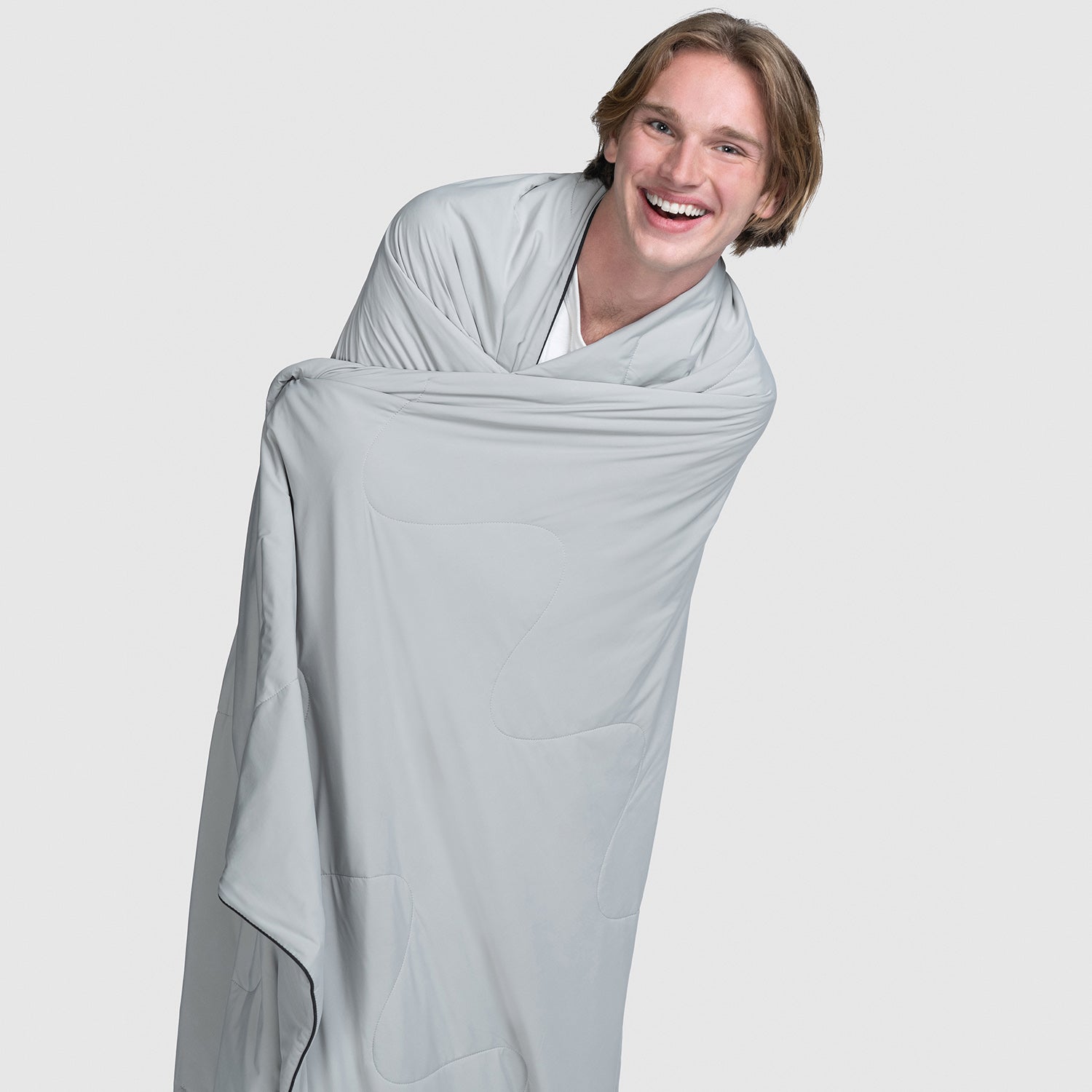 Smiling young man wrapped in a grey blanket against a plain background
