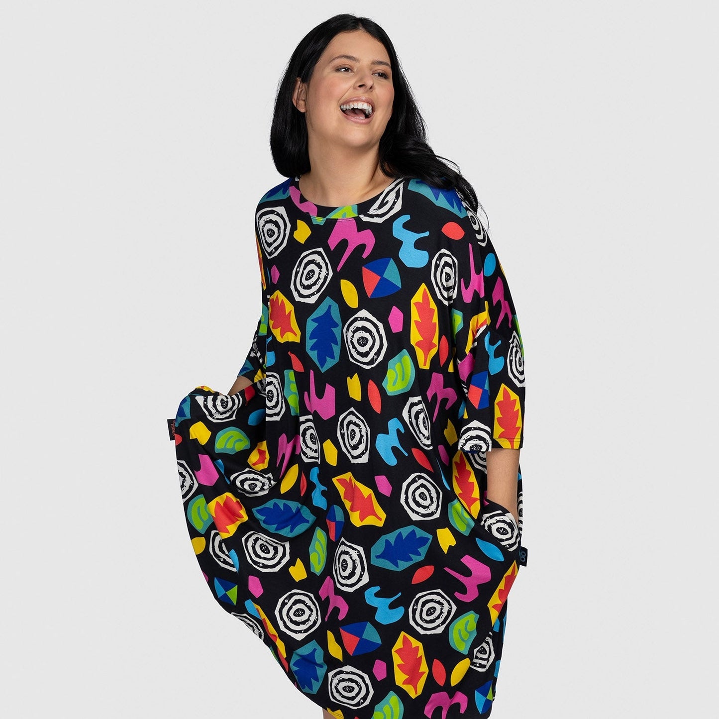 Woman smiling wearing a colorful dress with abstract shapes and leaf patterns