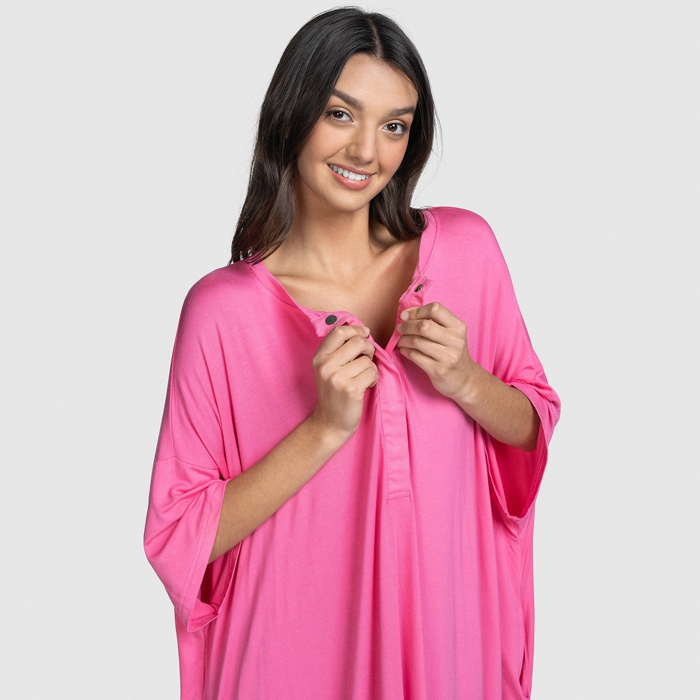 Smiling woman wearing a bright pink loose-fitting top, holding the neckline with both hands.