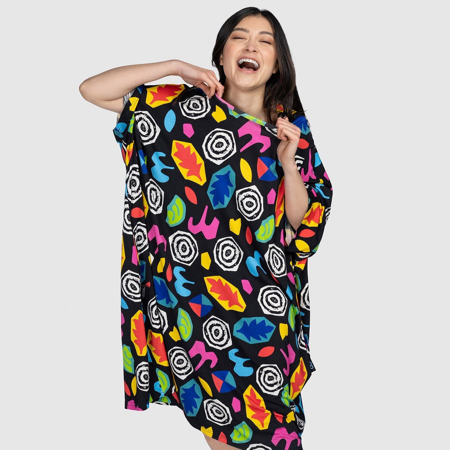 Woman smiling and holding a colorful garment with abstract leaf and swirl patterns on a black background