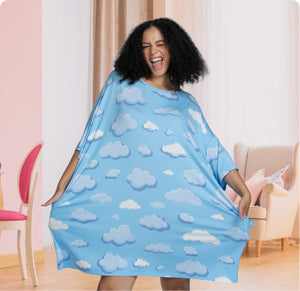 Person wearing a blue dress with white cloud patterns, smiling and holding the dress out