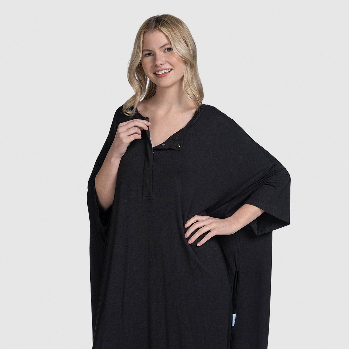 Woman wearing a loose-fitting black button-up top with 3/4 length sleeves and a snap button near the neckline, smiling with one hand on her hip.