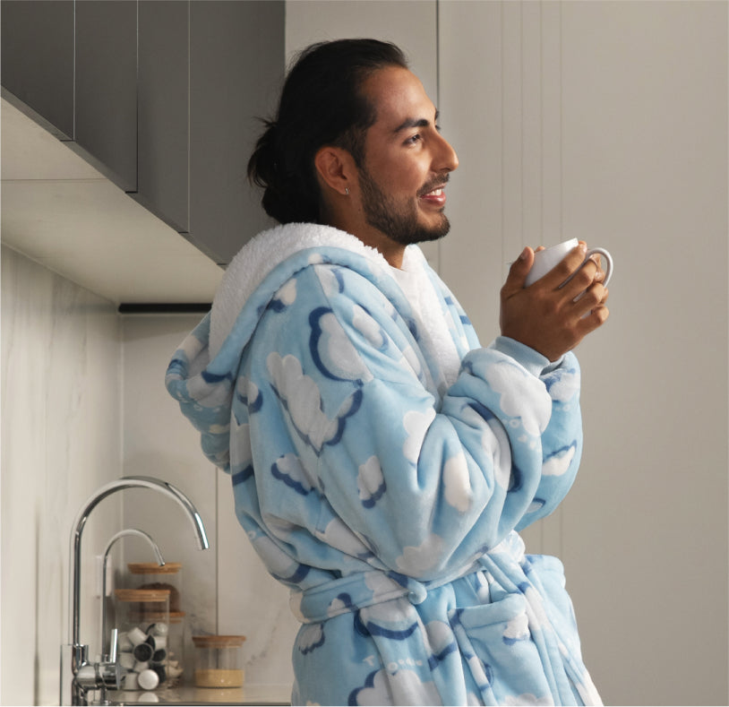 Man wearing a blue cloud-patterned robe holding a white mug in a kitchen