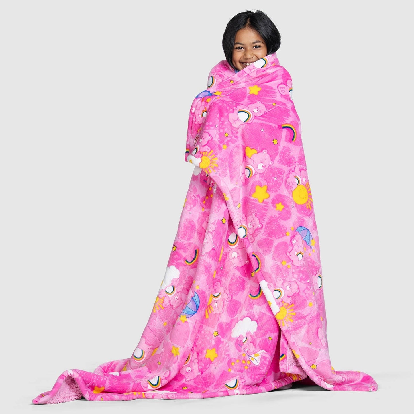 Girl wrapped in a pink Care Bears blanket with stars, rainbows, clouds, and suns pattern