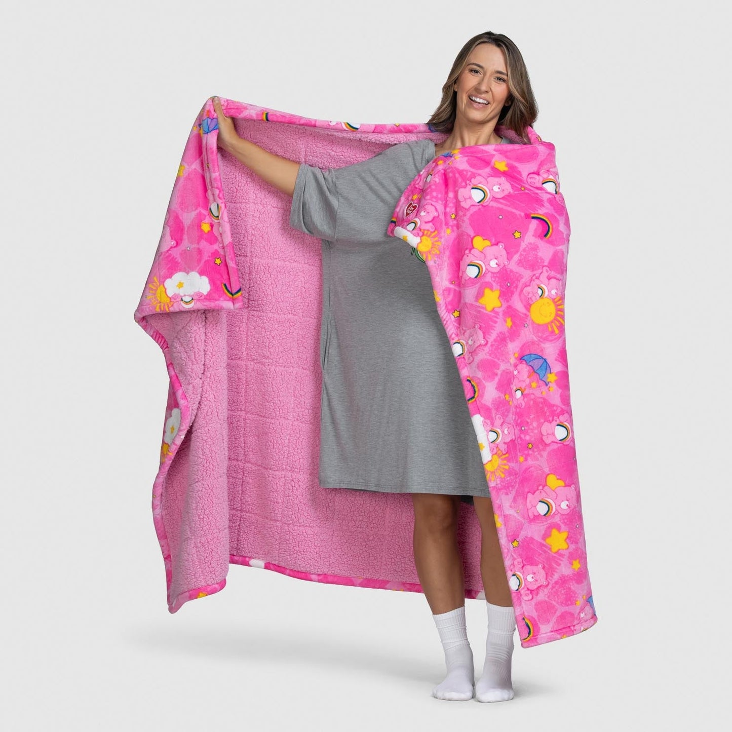 Woman holding a pink Care Bears blanket with colorful patterns including stars, suns, and clouds