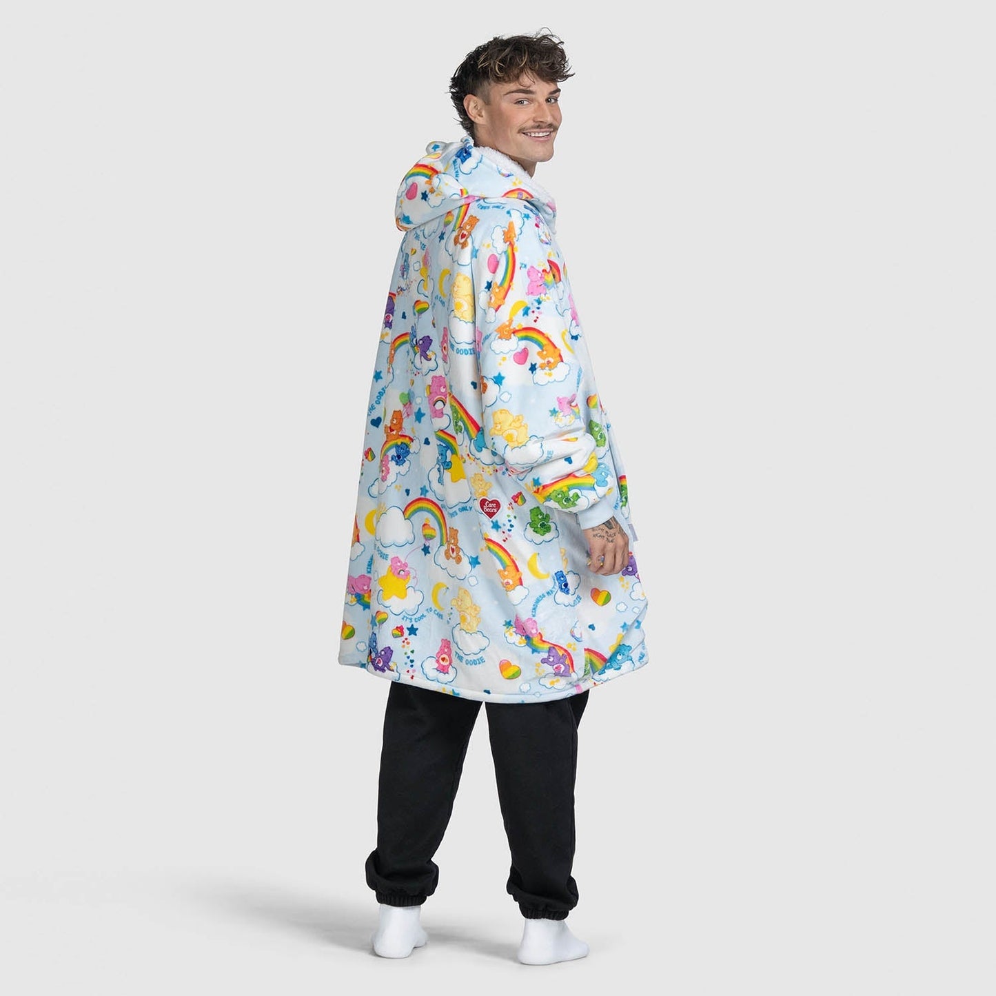 Man wearing a colorful hooded garment with Care Bears and clouds pattern, standing and looking over his shoulder