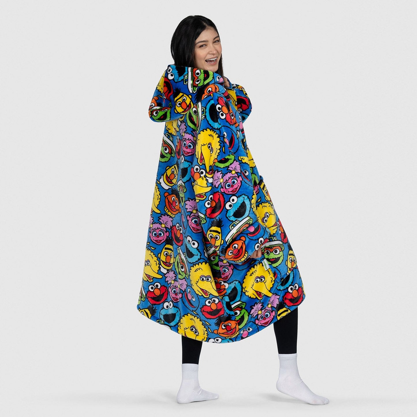 Woman smiling over her shoulder wearing a colorful Sesame Street character-print hooded garment, standing with white socks; Shanti is 5'2
