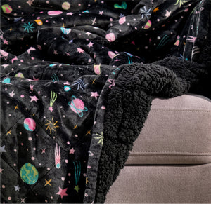Black fleece blanket with colorful space-themed patterns draped over a beige couch armrest
