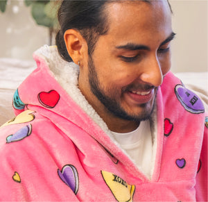 Man smiling wearing a pink hooded Oodie with colorful heart and candy designs