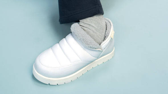 White slip-on slipper with fleece lining worn with gray socks on light blue floor