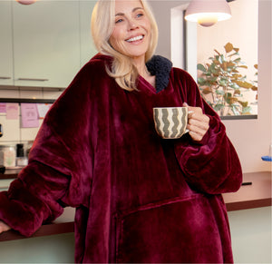Woman wearing a burgundy plush oversized hoodie holding a mug in a kitchen setting
