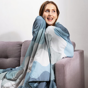 Woman wrapped in a blue and gray patterned blanket sitting on a gray couch, smiling