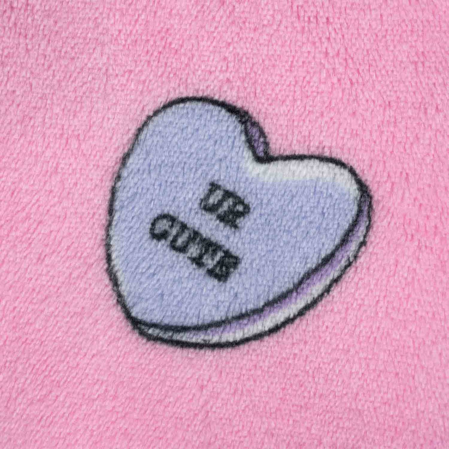 Purple heart-shaped candy with the words 'UR CUTE' on a pink textured background
