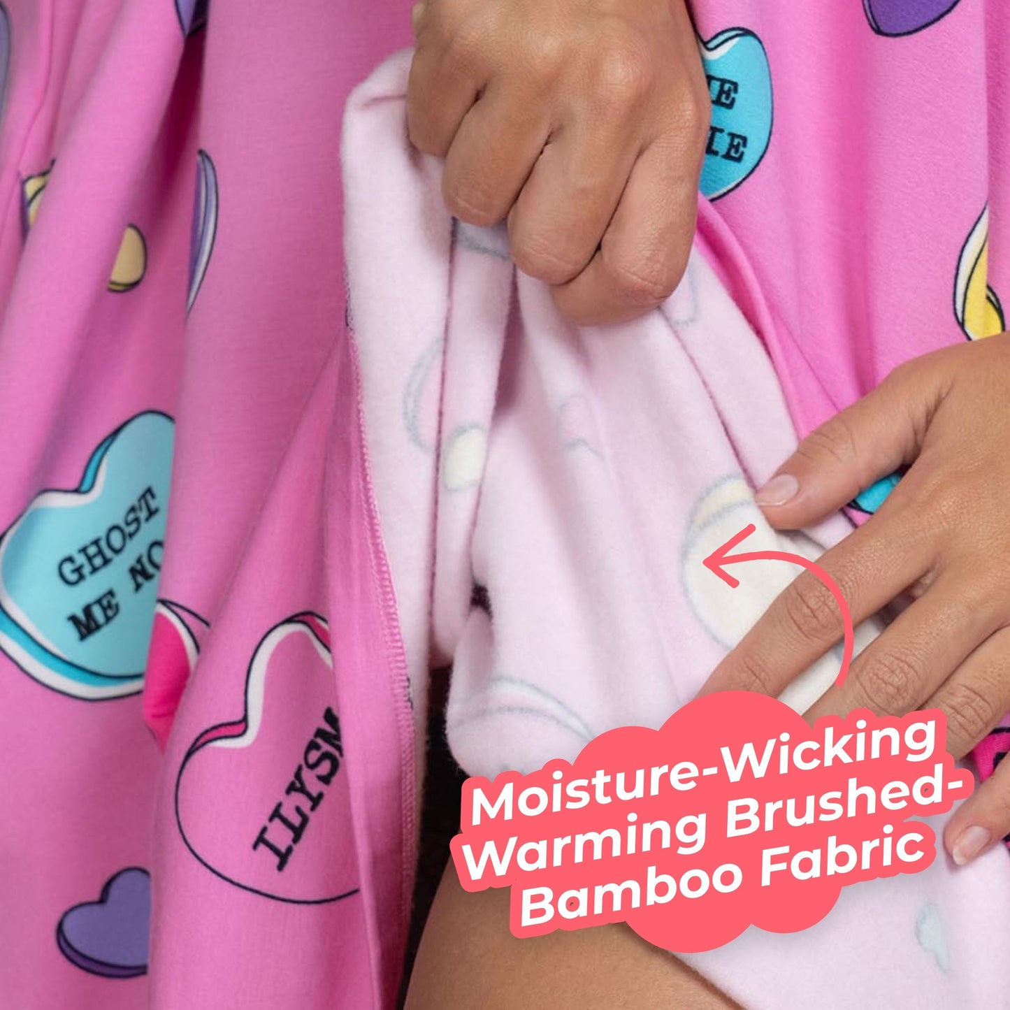 Hands holding pink fabric printed with conversation hearts saying 'GHOST ME NOT', 'ILYSM', and 'LOVE CANDY'. Text overlay reads 'Moisture-Wicking Warming Brushed-Bamboo Fabric'.