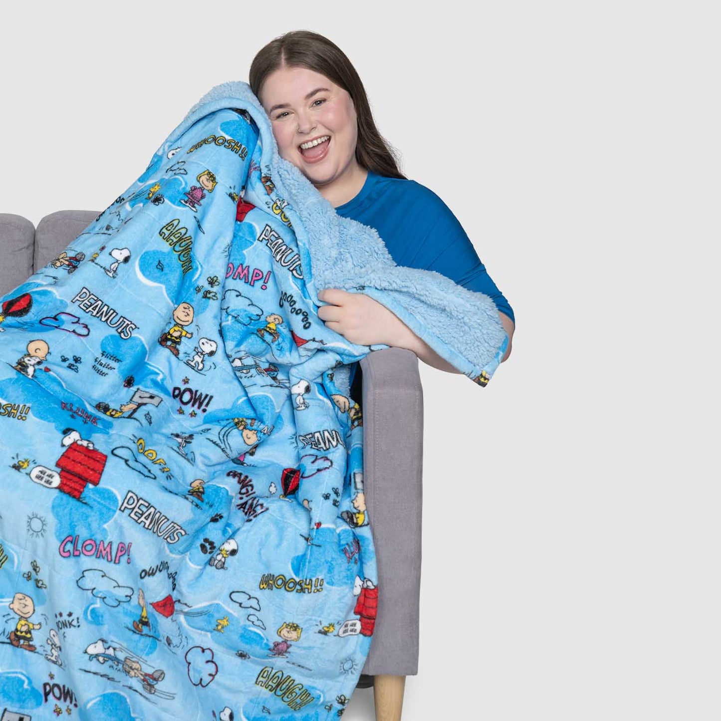 A smiling woman holding a blue Peanuts-themed blanket with cartoon characters and comic-style words like POW, CLUMP, and PEANUTS.
size: Lucy is 5'9