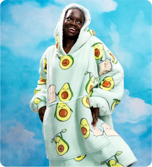 Smiling person wearing a light green oversized hoodie with avocado and toast prints against a blue sky background
