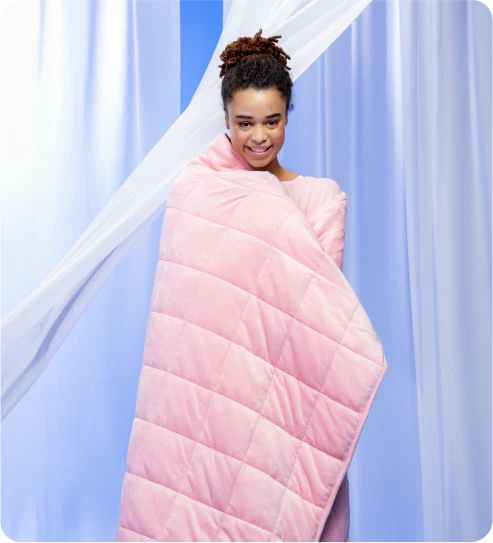 Young woman wrapped in a pink quilted blanket against a light blue background