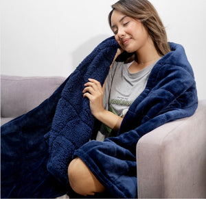 Woman wrapped in a navy blue plush blanket sitting on a couch, smiling with eyes closed