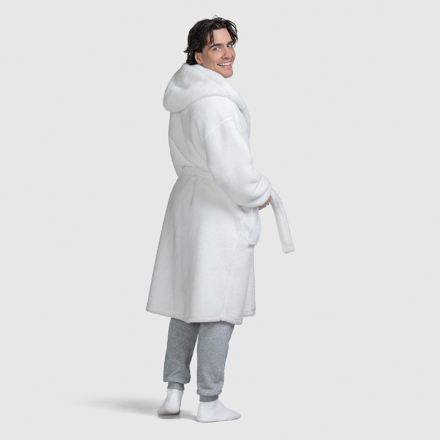 Man wearing a white hooded bathrobe, standing and looking back with a smile.
