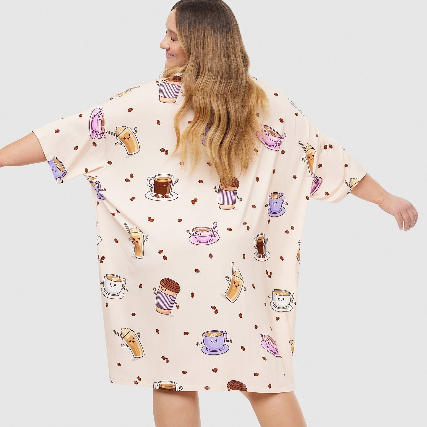 Woman wearing a cream-colored dress with colorful coffee cup illustrations all over it, viewed from the back with arms outstretched.