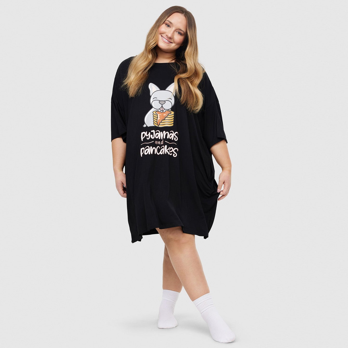 Woman wearing a black nightshirt with a cartoon bulldog holding pancakes and the text 'pyjamas and pancakes'