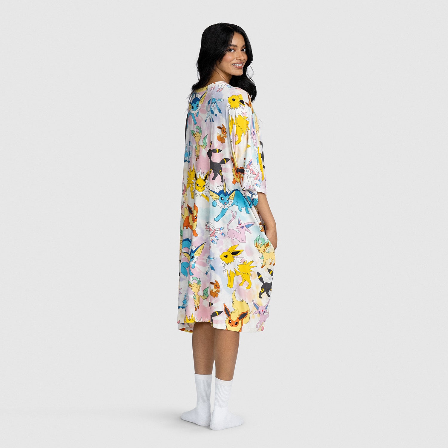 Woman wearing a dress printed with colorful Pokémon Eevee evolutions characters, standing and looking over her shoulder.