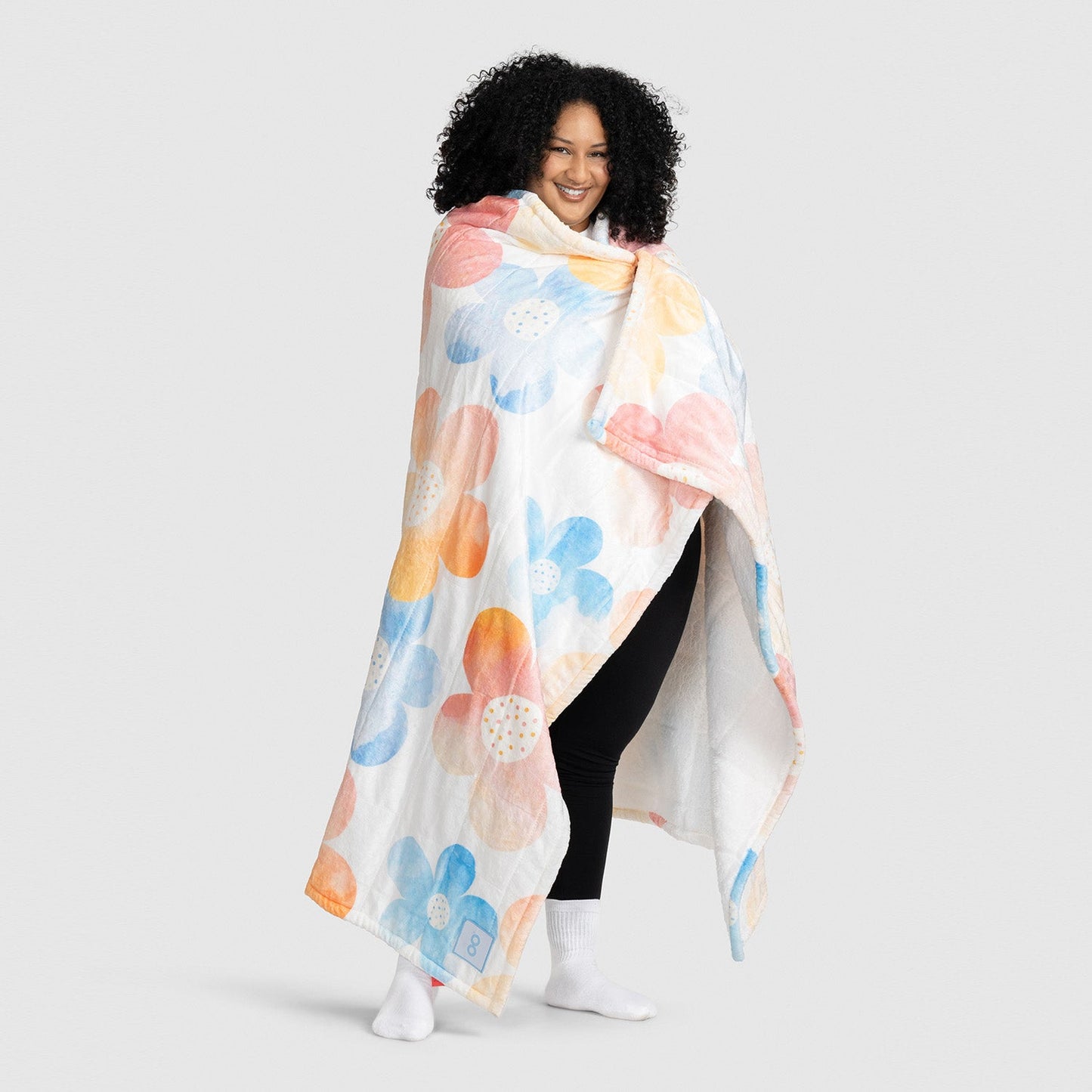 Person wrapped in a white blanket with large pastel floral patterns in blue, orange, and pink.