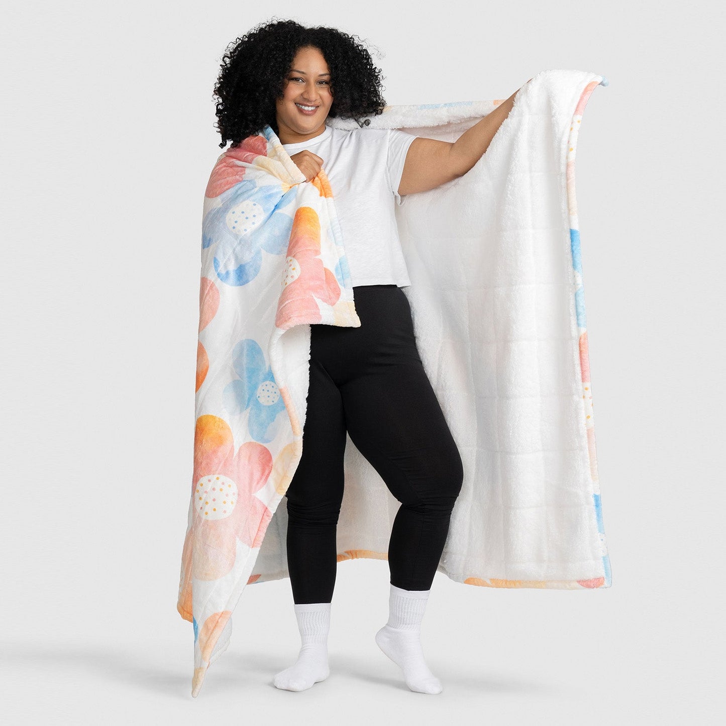 Woman holding a large blanket with a colorful floral pattern, showing both the patterned and white sides