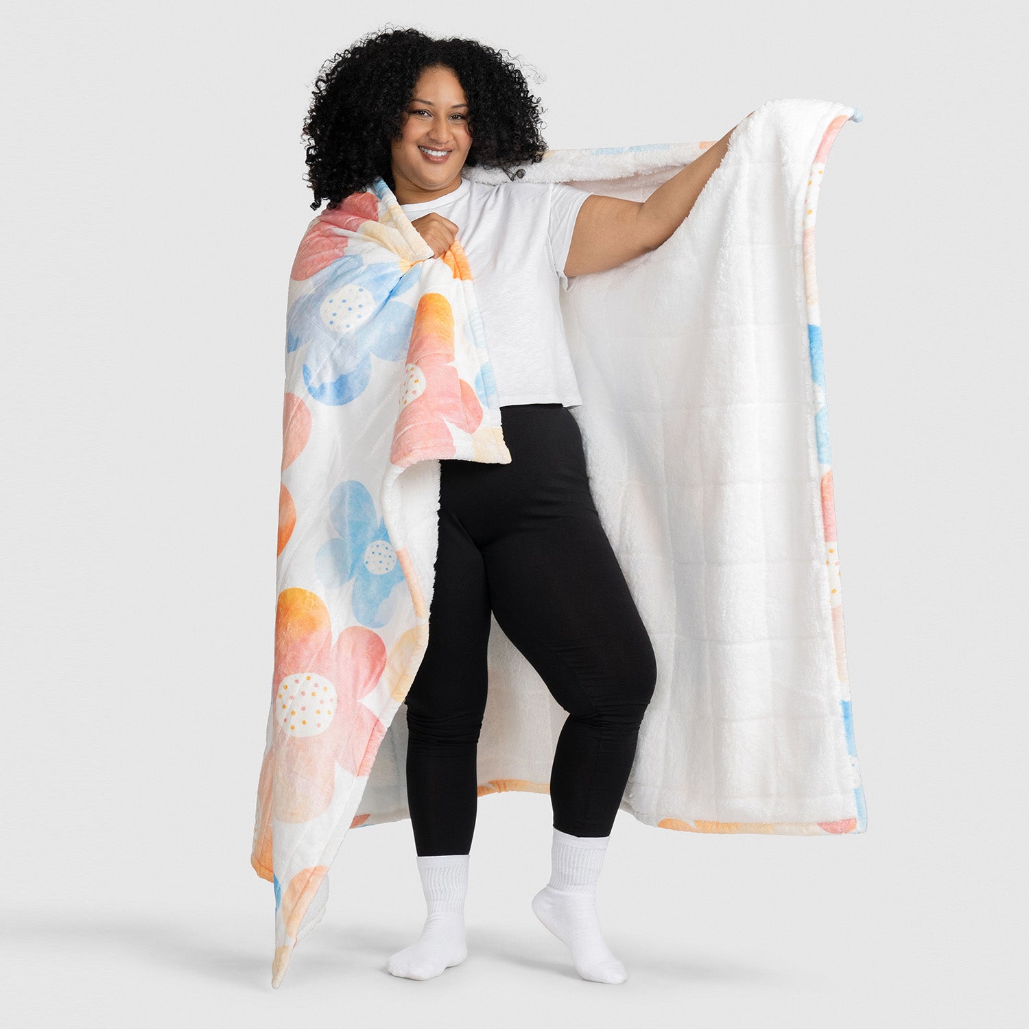 Woman holding a large blanket with a colorful floral pattern, showing both the patterned and white sides