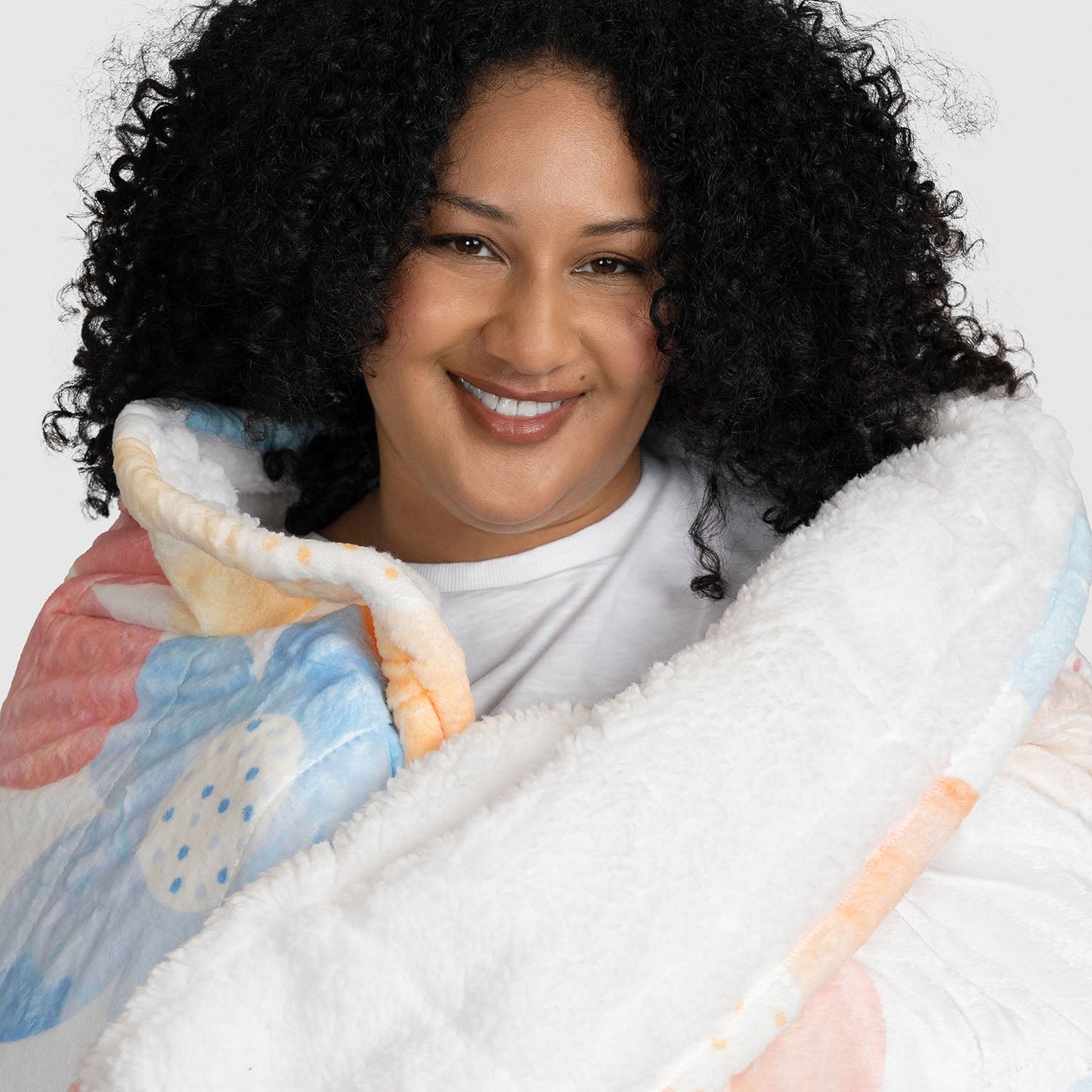 Smiling woman wrapped in a colorful floral-patterned blanket with white fleece lining