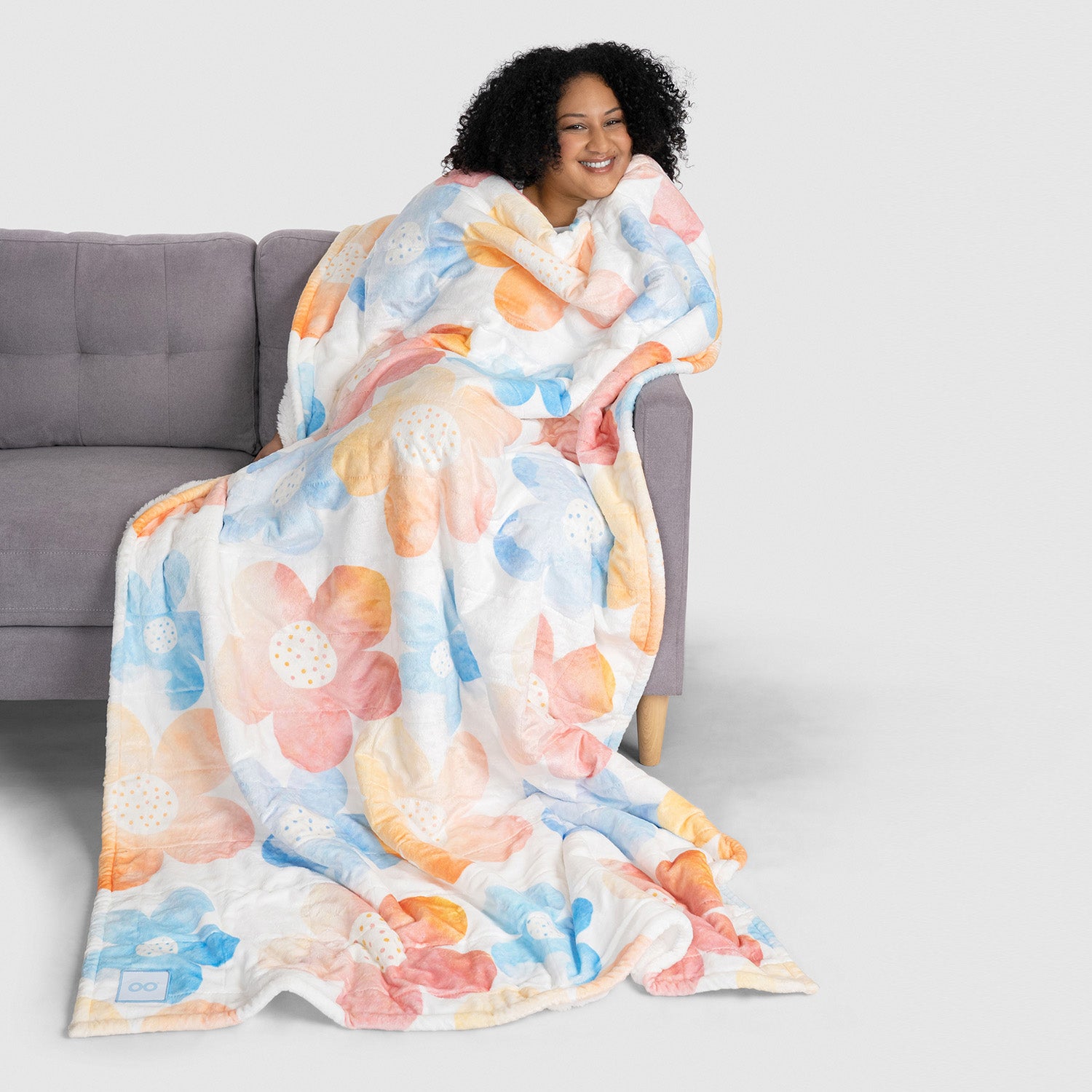 Smiling woman wrapped in a large floral-patterned blanket sitting on a gray couch