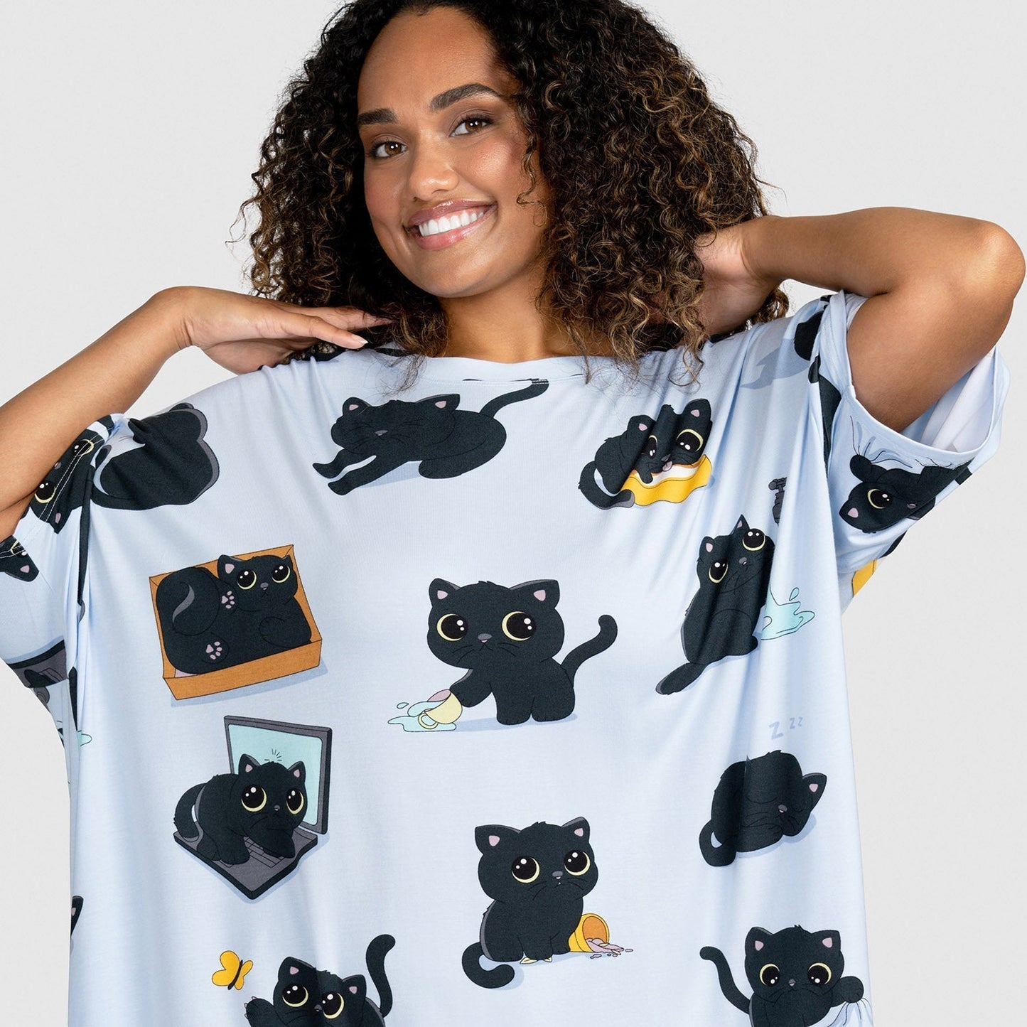Woman wearing a light blue shirt with multiple cartoon black cats in various playful poses printed all over it.